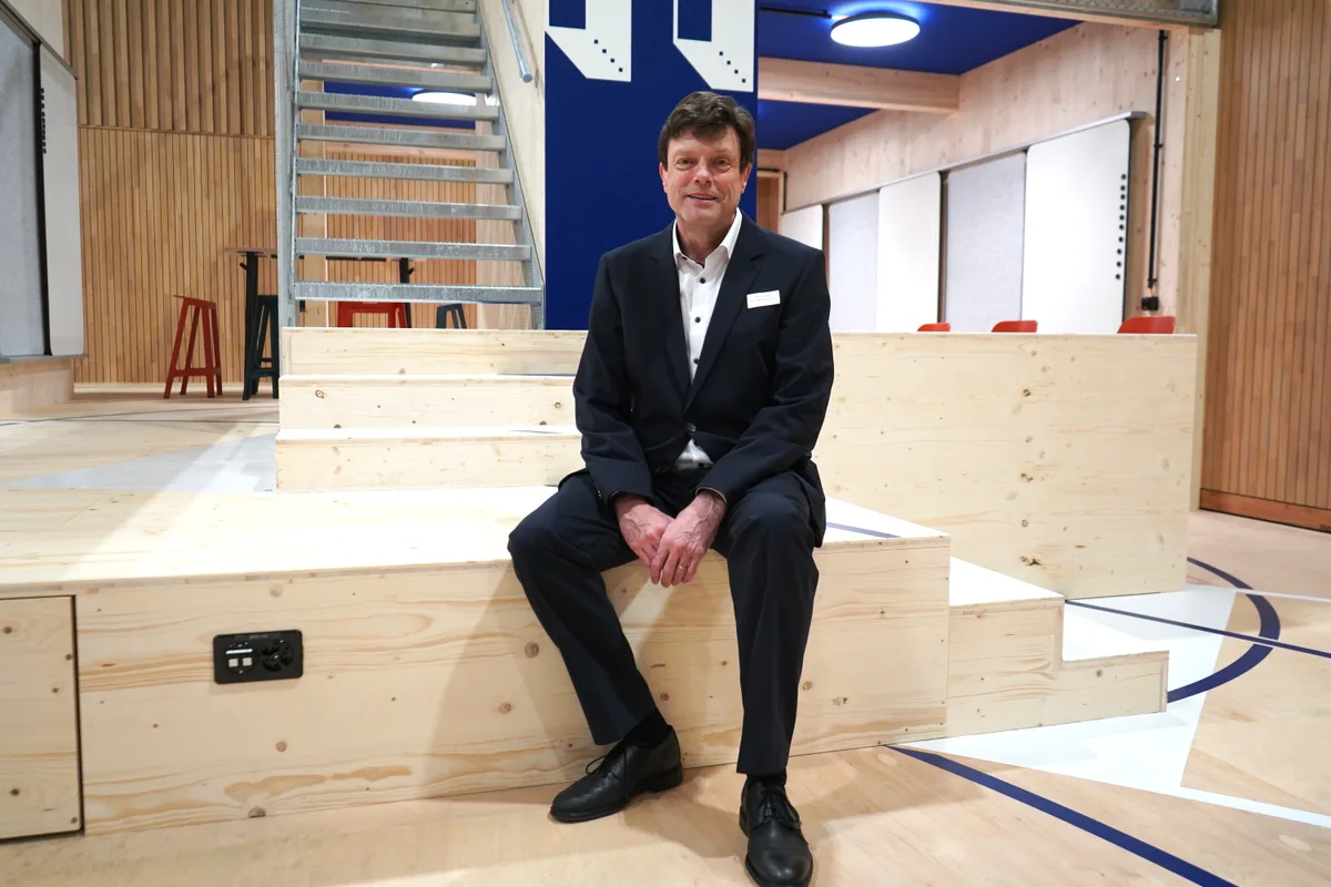 Otto Schlosser sitzt auf einer Treppe aus hellem Holz. Er trägt einen dunklen Anzug und ein helles Hemd.